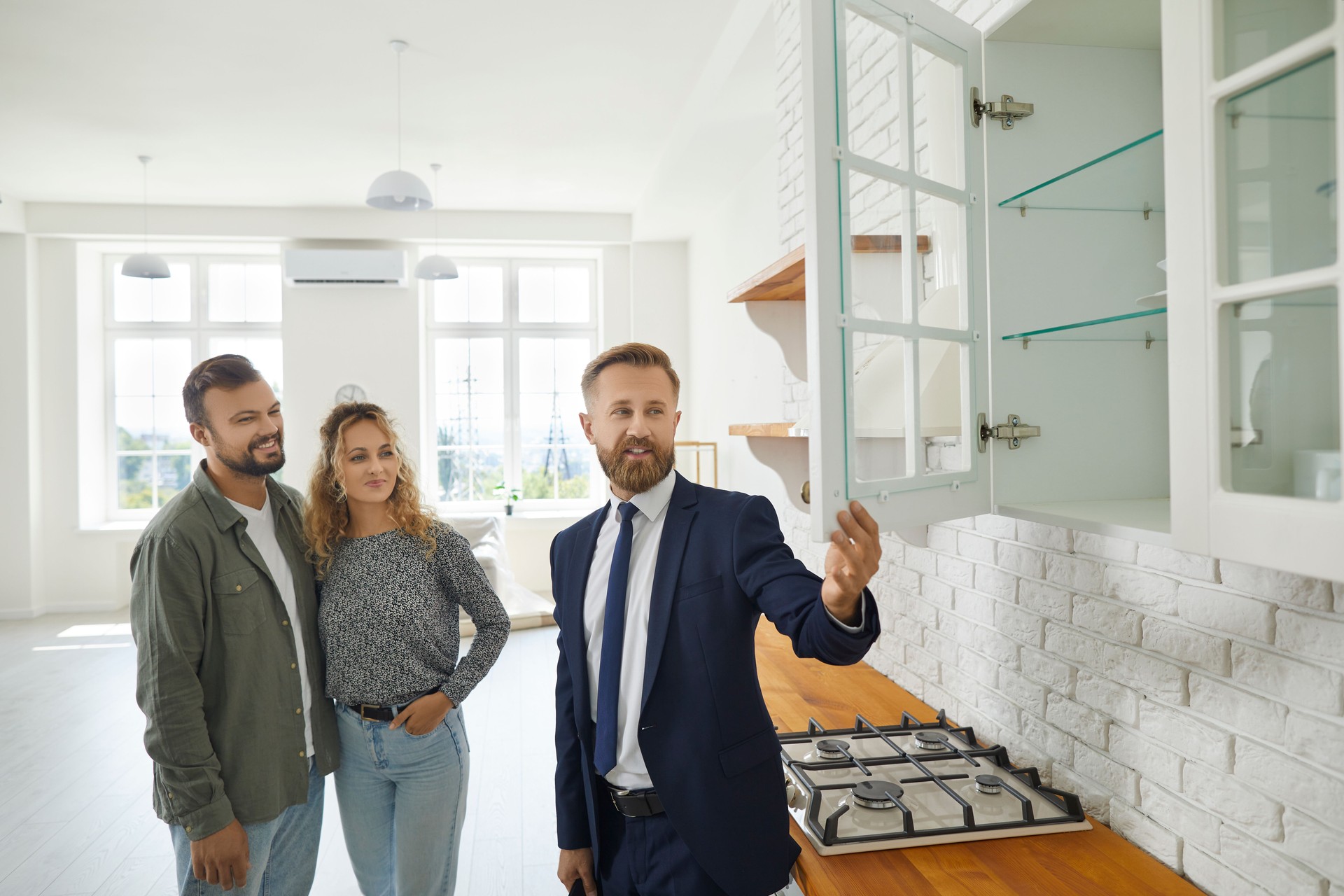 Real estate agent showing buyers kitchen cabinets while giving tour about new house